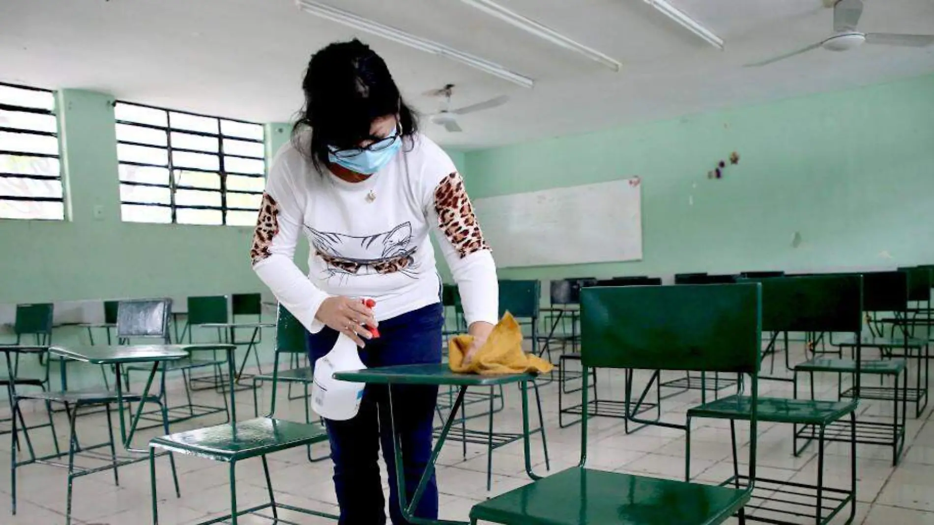 Mujer limpiando pupitres en un salón de clases